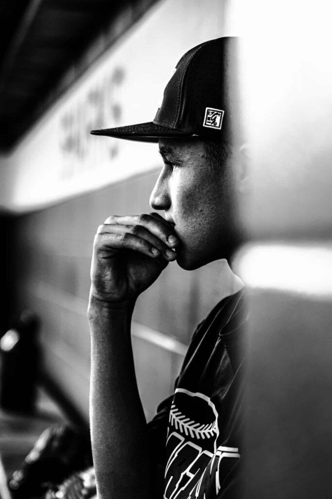 Un joven con gorra de béisbol, sentado de perfil, apoya la barbilla en la mano y se muestra pensativo. La foto en blanco y negro subraya su expresión contemplativa, como si reflexionara sobre la información tech o las tendencias del sector tecnológico.