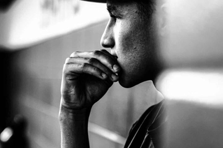 Un joven con gorra de béisbol, sentado de perfil, apoya la barbilla en la mano y se muestra pensativo. La foto en blanco y negro subraya su expresión contemplativa, como si reflexionara sobre la información tech o las tendencias del sector tecnológico.